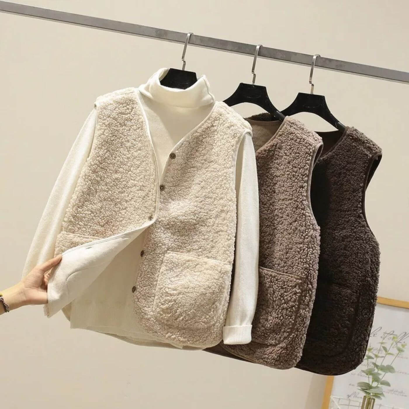 Gilets sans manches en fausse fourrure pour femmes en beige, marron et brun foncé, avec boutons et poches avant, suspendus sur des cintres.