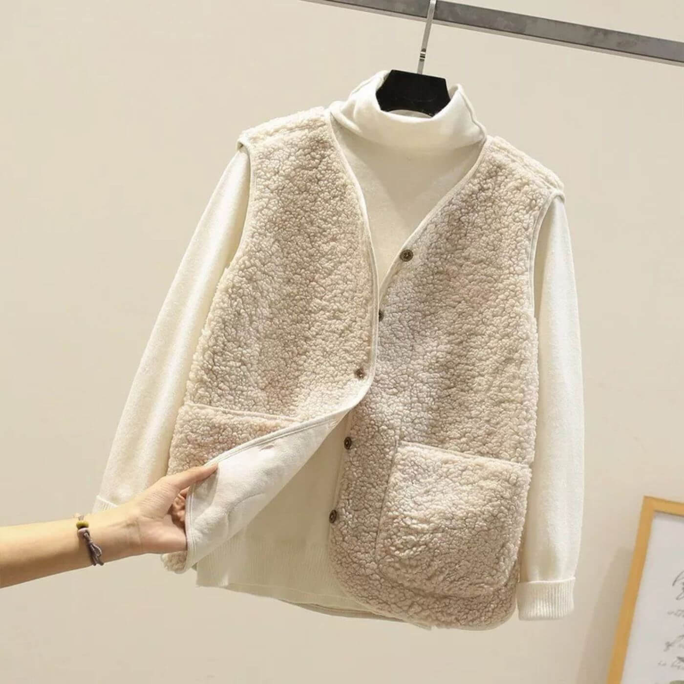 Gros plan d'un gilet en fausse fourrure beige sur un col roulé blanc, mettant en valeur la texture douce et les détails des boutons.