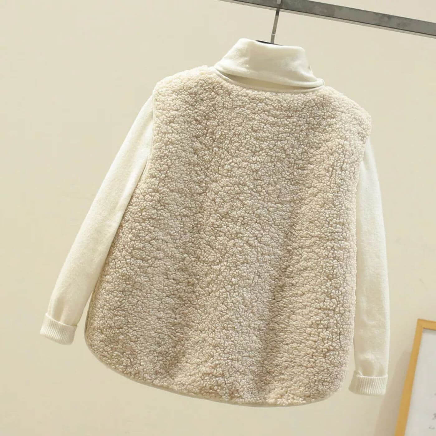 Vue arrière d'un gilet en fausse fourrure beige, montrant un matériau lisse et confortable.