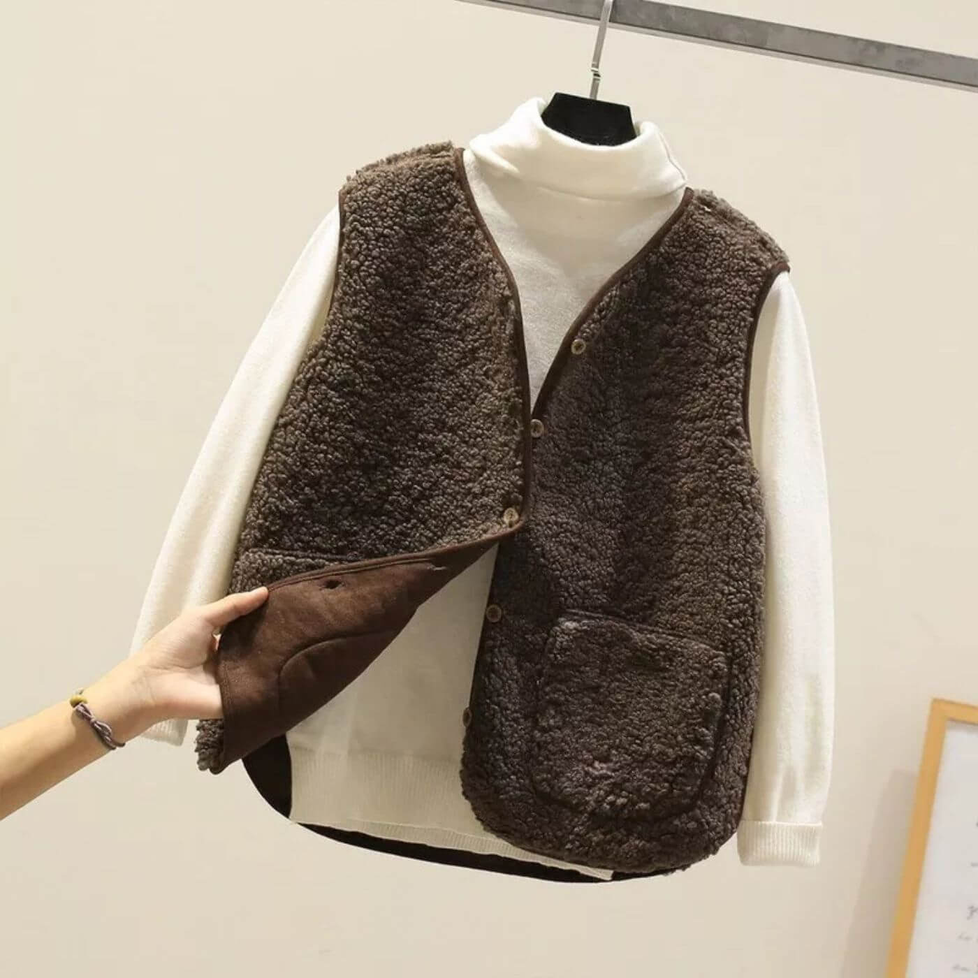 Gilet brun foncé en fausse fourrure associé à un col roulé blanc, soulignant son design chaud et élégant.